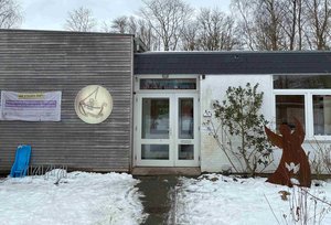 Ein einstöckiges Gebäude im Schnee. Links neben der Tür hängt ein Logo