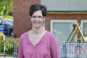 Eine Frau mit braunen kurzen Haaren und Brille sowie einem pinken Oberteil