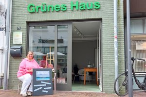 Eine Frau sitzt vor einem Haus mit geöffneter Tür und der Aufschrift "Grünes Haus"