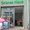 Eine Frau sitzt vor einem Haus mit geöffneter Tür und der Aufschrift "Grünes Haus"