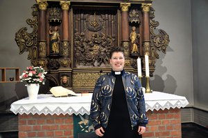 Eine junge Frau mit Brille und kurzen dunklen Haaren steht vor einem Altar