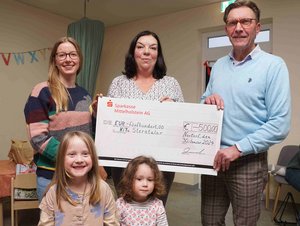 Zwei Frauen und ein Mann halten einen überdimensionalen Scheck, im Vordergrund zwei Kinder