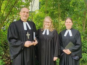 Zwei Frauen und ein Mann im Talar lächeln in die Kamera