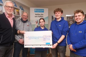 Zwei Erwachsene und drei Jugendliche in blauen Pullis zeigen einen überdimensionalen Scheck