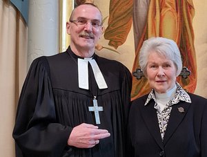 Ein Mann in schwarz mit umgehängtem Kreuz und eine ältere Frau