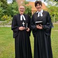 Propst Krüger und Pastorin Andersson stehen auf einer Wiese, im Hintergrund die Hohner Kirche