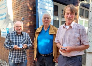 Drei Männer stehen vor einem Haus mit der Infotafel der Diakonie Rendsburg-Eckernförde.