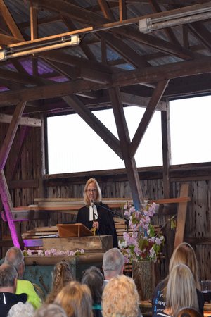 Eine Frau in schwarzem Talar spricht hinter einem Altar stehend mit davor sitzenden Menschen