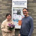 Ein Mann und eine Frau mit Blumen in der Hand stehen vor einem Schild an einer Häuserwand