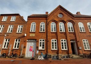 Ein Gebäudeensemble mit zwei roten Backsteingebäuden, die wie Wohnhäuser aussehen.