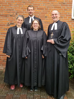 Zwei Frauen und zwei Männer in Talaren lächeln in die Kamera