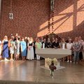 Eine große Gruppe Menschen steht im sonnigen Vorraum einer Kirche