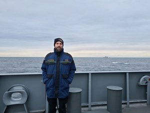 Ein Mann an der Reling eines Marineschiffes, im Hintergrund das offene Meer