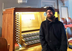 Ein Mann sitzt mit Mütze und Jacke vor einer beleuchteten Orgel