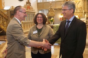Im Vordergrund schütteln zwei Männer Hände, im Hintergrund eine Frau.