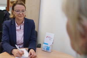 Eine Frau sitzt an einem Tisch in einem Büro und notiert etwas mit einem Stift