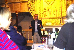 Ein Mann spricht zu im Vordergrund sichtbaren, sitzenden Menschen