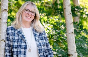 Eine Frau steht bei schönem Wetter an einen Baum gelehnt.