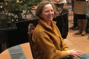 Eine Frau mit halblangen Haaren und einer Brille sitzt auf einem Stuhl und lächelt in die Kamera