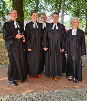 Fünf Menschen in geistlicher Kleidung stehen vor Bäumen und lächeln in die Kamera