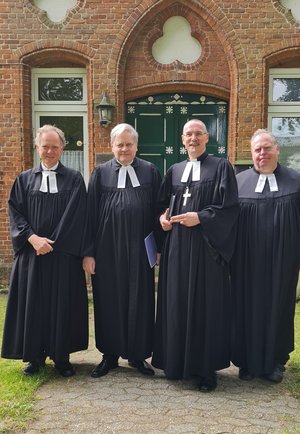 Vier Männer im Talar vor einem Kirchgebäude