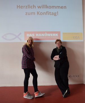 Zwei Frauen lehnen an einer Wand, auf die eine Folie projiziert wird