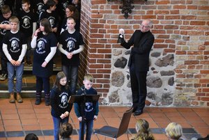 Ein Mann mit einer Glocke in der Hand, mehrere Kinder mit gleich aussehenden T-Shirts