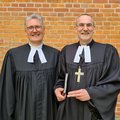 Zwei Männer im schwarzen Talar, einer hat ein Kreuz umgehängt