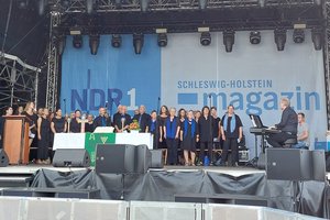 Ähnlich gekleidete Menschen stehen auf einer Bühne und singen