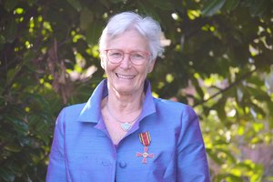 Eine Frau steht vor einem Busch. An ihrer Jacke ist das Bundesverdienstkreuz am Bande befestigt.