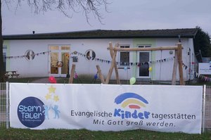 Außenansicht der Kita Sterntaler in Nortorf, im Vordergrund ein Banner mit der Aufschrift "Mit Gott groß werden"