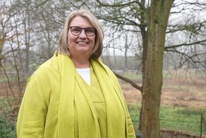 Eine blonde Frau in gelber Kleidung lächelt in die Kamera