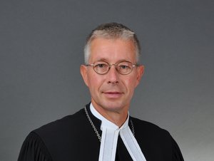 Ein Mann in Talar mit Beffchen, mit Brille und kurzen schwarz-weißen Haaren