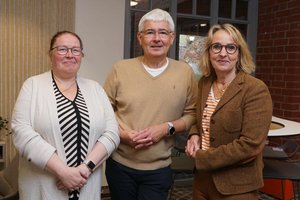 Ein Mann und zwei Frauen stehen an einem Stehtisch und lächeln in die Kamera.