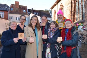 Sieben Menschen stehen in Winterkleidung vor einer Kerze und halten Holzschilder mit der Aufschrift "Würde unantastbar"