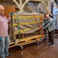 Drei Männer stehen in einem Kirchraum, in der Mitte ein verpackter Kasten