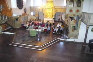 Aus der Vogelperspektive Blick in den Altarraum einer Kirche, in dem Menschen an Tischen sitzen