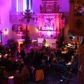 Viele Menschen sitzen an Tischen im Altarraum einer Kirche, der pink beleuchtet ist